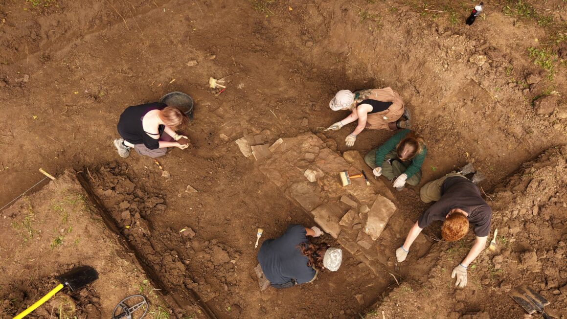 Archeolodzy prowadzą wykopaliska w dużym wykopie w Szczawnem, odsłaniając kamienne fundamenty dawnej cerkwi.