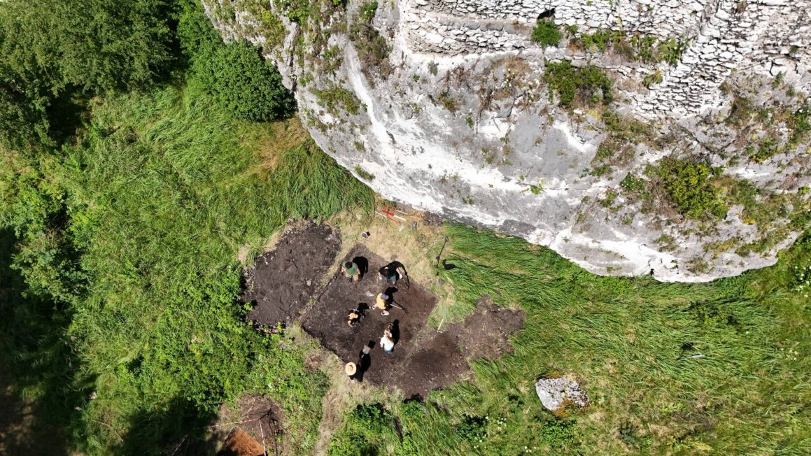 Widok z drona na archeologów pracujących w wykopie przy pionowej ścianie wapiennego ostańca w Przewodziszowicach.