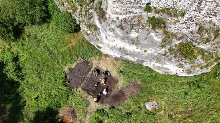 Widok z drona na archeologów pracujących w wykopie przy pionowej ścianie wapiennego ostańca w Przewodziszowicach.
