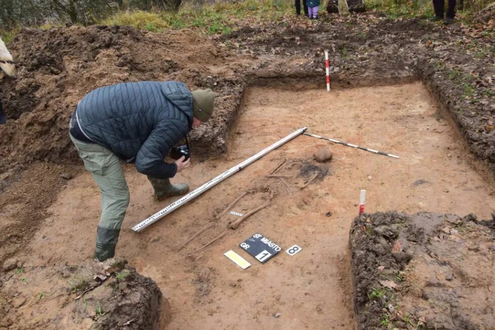 Archeolog dokumentuje szkielet ludzki odkryty w wykopie na średniowiecznym cmentarzysku w pobliżu Dąbrówna