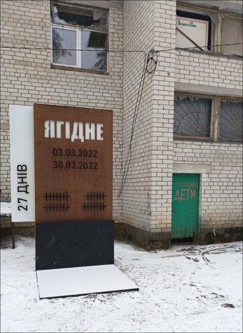 Pomnik ofiar zbrodni wojennej „27 dni. Jahidne”. Widoczne w tle drzwi, oznaczone czerwonym napisem „Uwaga. Dzieci”, prowadzą do piwnicy, w której więziono mieszkańców wsi, 1 marca 2025 (fot. G. Kiarszys).