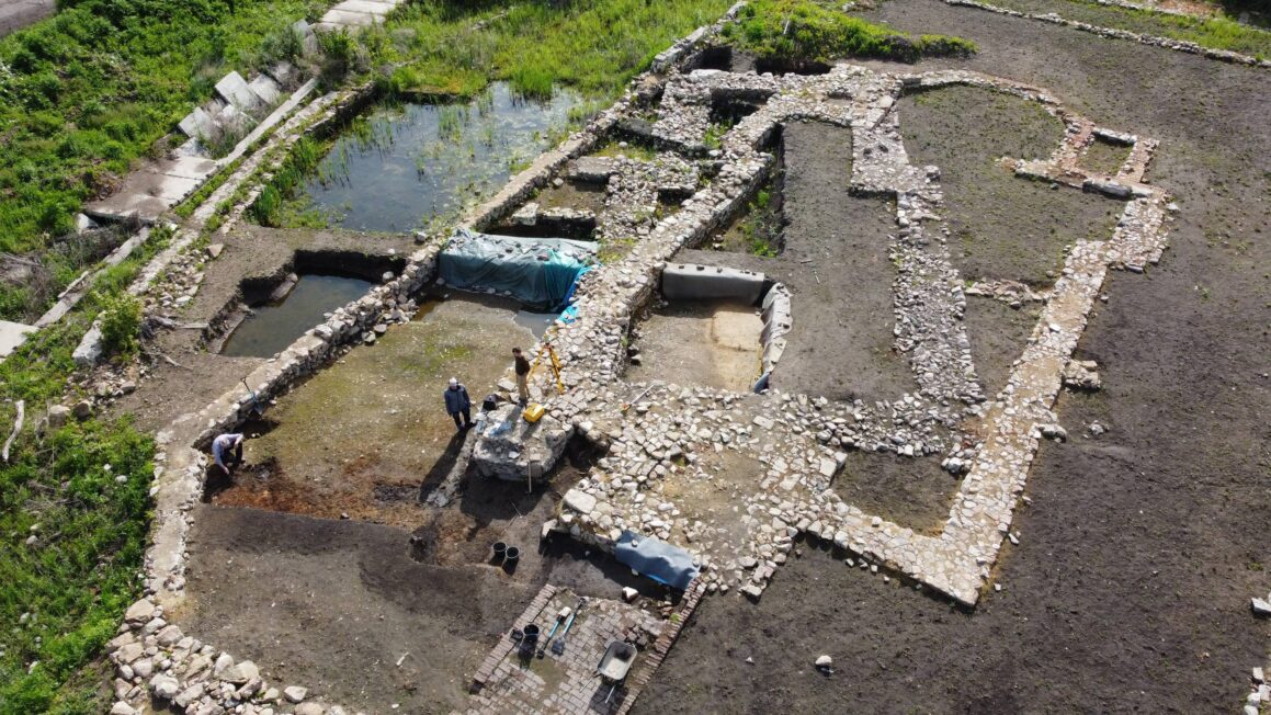 Widok z góry na wykopaliska średniowiecznego kościoła w Libkovicach, z odsłoniętymi kamiennymi i ceglanymi murami oraz archeologami pracującymi między reliktami