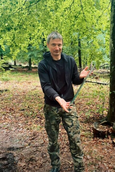 Mężczyzna stojący w lesie trzyma długi, zielonkawy miecz z brązu po jego wydobyciu